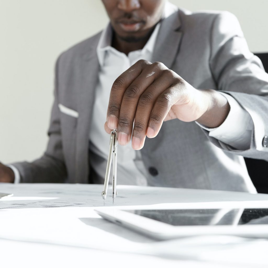 African engineer using technical drawing tool for calculating measurements of housing project. Black